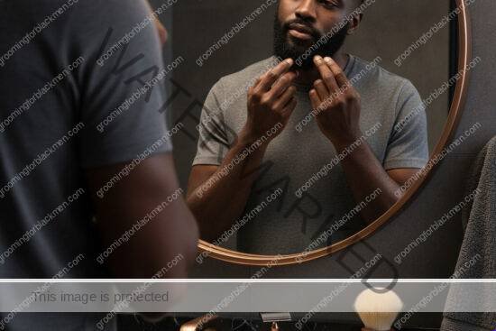 Black man with rich brown skin checking beard direction before shaving