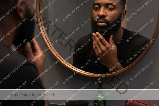 Black man calmly checking his beard before deciding shaving frequency