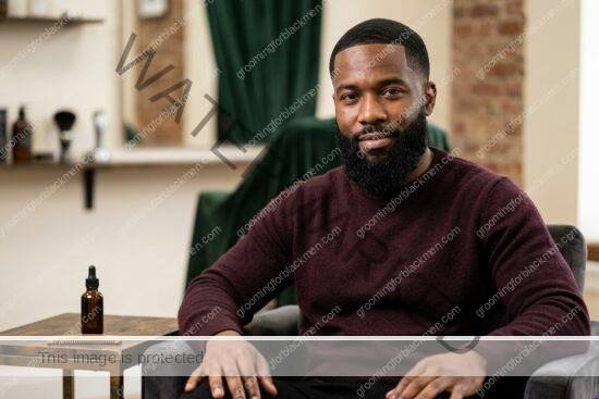 Black man with rich brown skin using affordable beard oil in a premium grooming setting