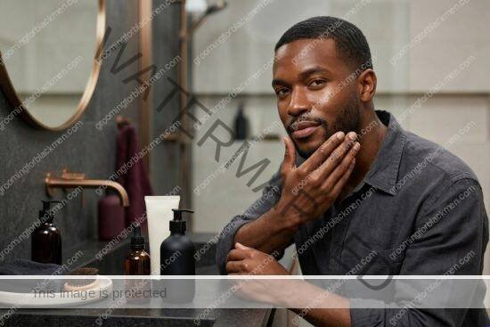 Black man with rich brown skin using affordable moisturizer in a premium grooming setting