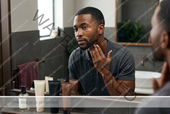 Black man with rich brown skin reviewing affordable skincare products at a bathroom sink