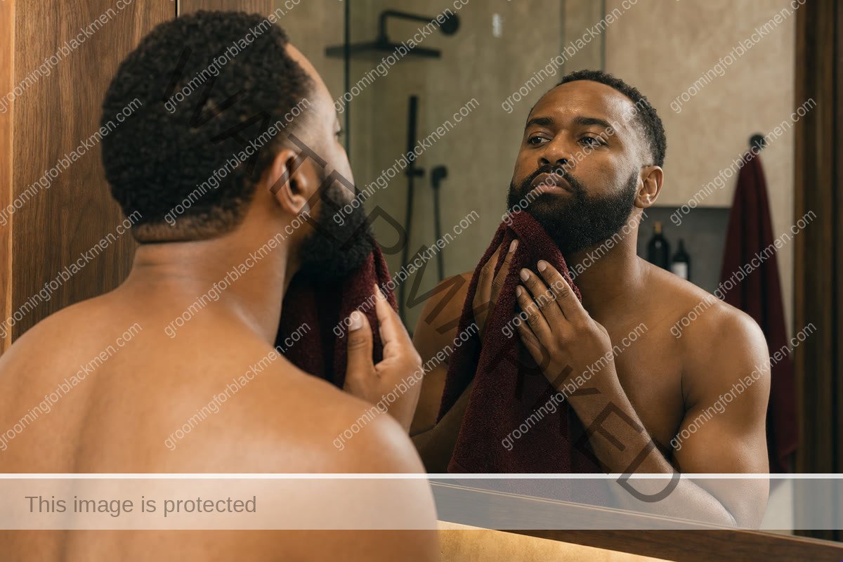 Black man gently drying his beard with a towel before applying grooming product
